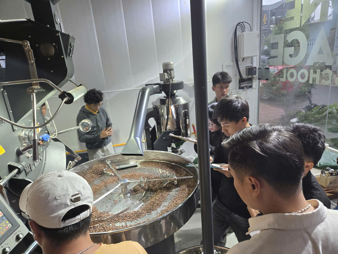 Mẻ cà phê rang thử nghiệm đang đảo trên khay làm nguội, học viên ghi chép thông số