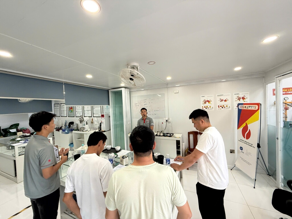 Học viên đứng quanh bàn thực hành với bát cupping, cốc đong và phiếu ghi.