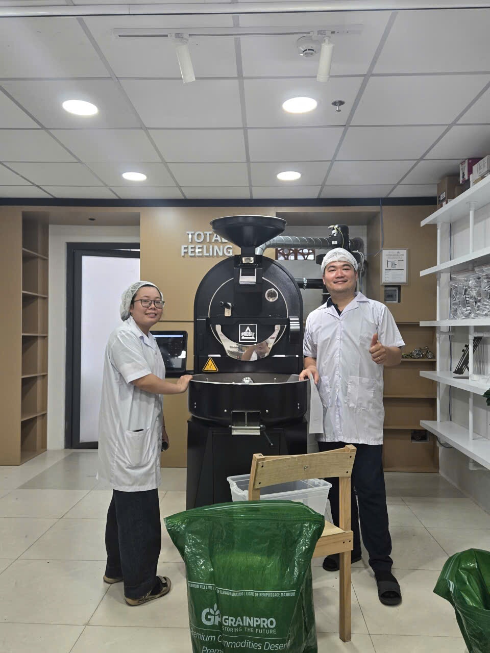 Hai người bên máy rang Probat tại Total Feeling, phía trước là bao GrainPro đựng cà phê nhân xanh