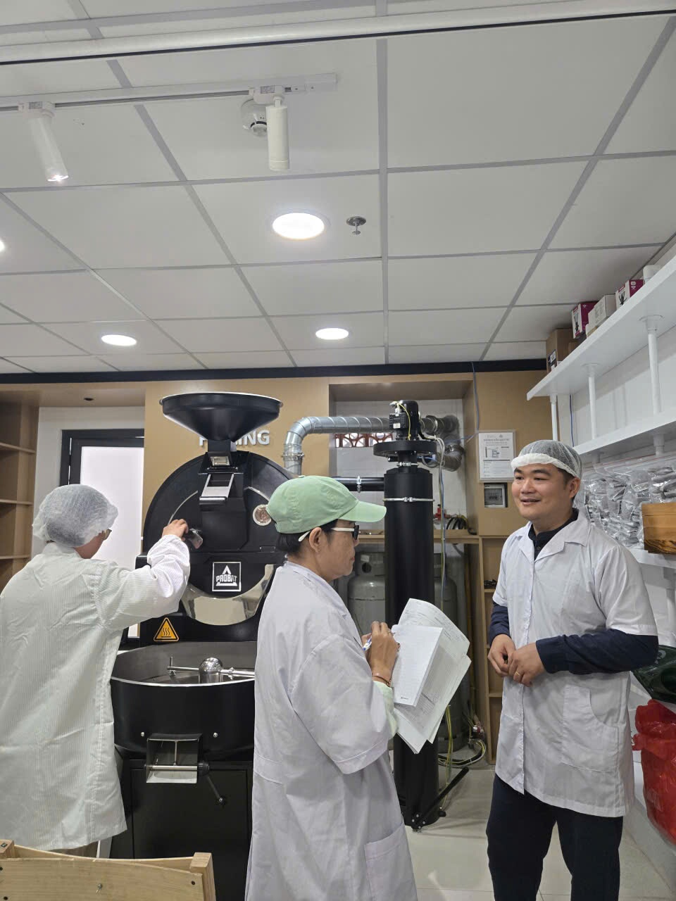 Phòng rang của lớp SCA Roasting tại TP.HCM với máy rang Probat, người trong phòng mặc áo blouse và mũ trùm tóc