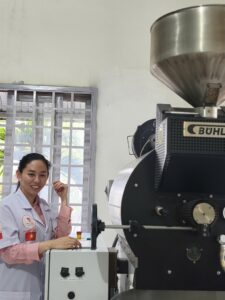 Máy rang cà phê công nghiệp Bühler với phễu nạp nhân xanh phía trên tại xưởng rang của học viên