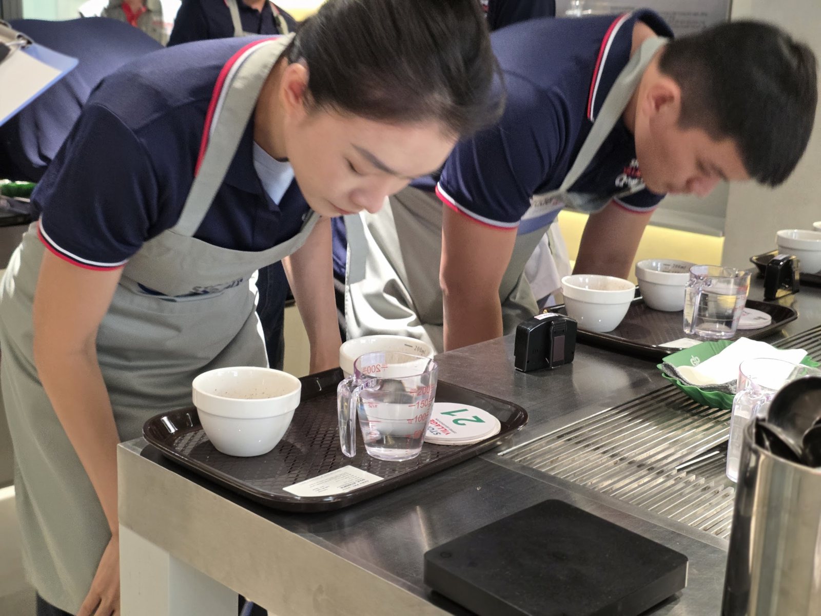 Hai học viên cảm nhận hương các chén mẫu trên bàn cupping