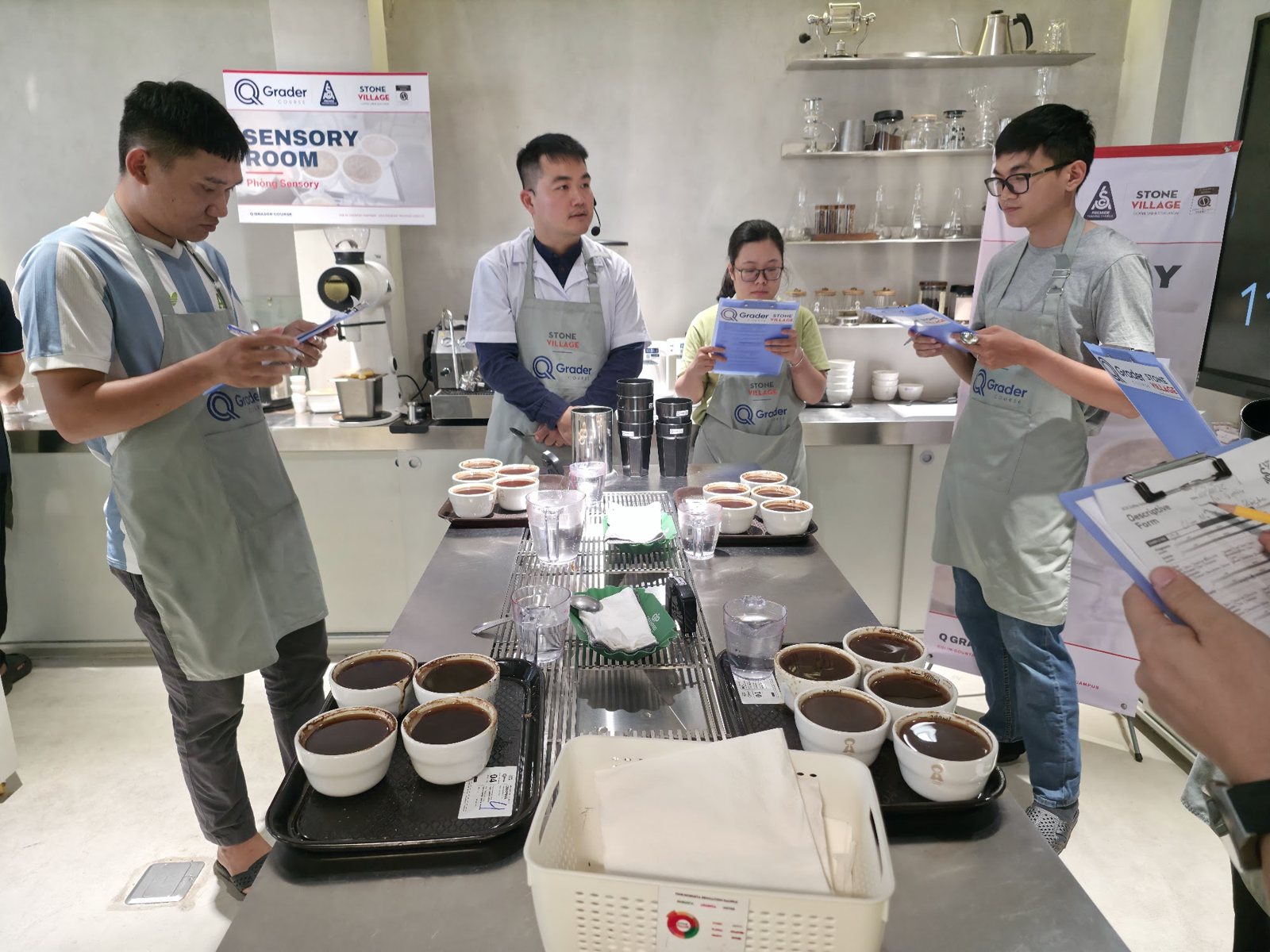 Học viên cầm biểu mẫu đứng quanh bàn cupping