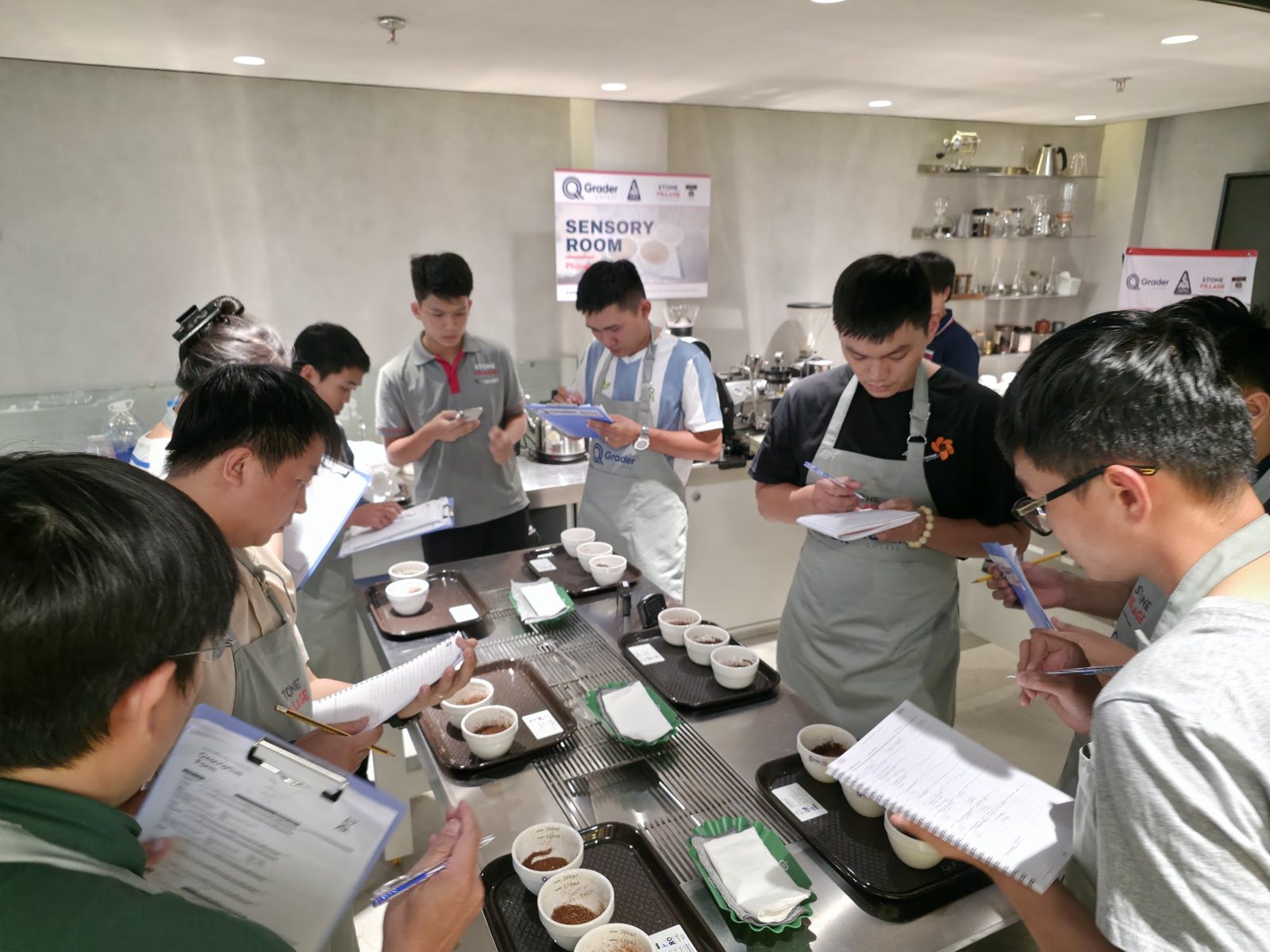 Học viên cầm bảng ghi đứng quanh bàn mẫu