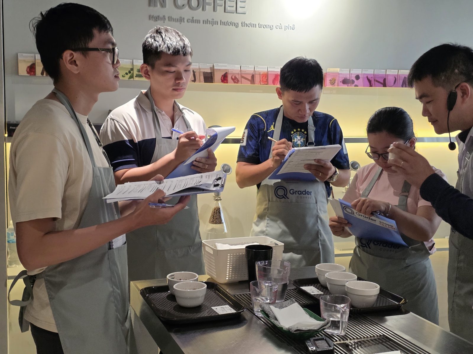 Nhóm học viên cầm bảng kẹp đánh giá mô tả bên bàn mẫu